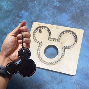 May include: Black leather Mickey Mouse keychain with white stitching, held by a hand. A wooden die-cut template in the shape of Mickey Mouse is in the background. The template has the date "2025.09.20" printed on it.