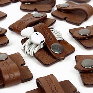 May include: Brown leather cord organisers with a magnetic closure and the word "Tophone" embossed on each. The organisers are designed to hold and organise cords, such as headphone cords.