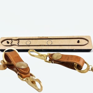 Könnte beinhalten: Zwei braune Leder-Schlüsselanhänger mit goldfarbener Hardware und eine Holzstanzschablone. Die Schlüsselanhänger haben einen münzförmigen Akzent. Die Holzschablone trägt den Text "TopHome".