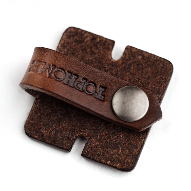 May include: A brown leather key chain with a metal button and the word "TOPHOL" embossed on the leather strap.
