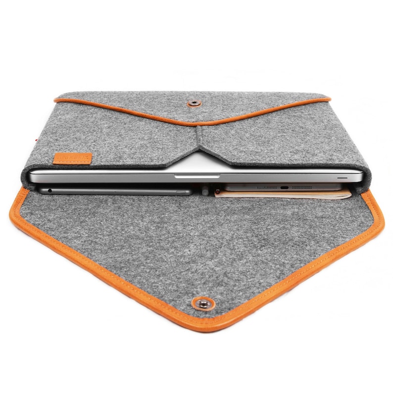 May include: Grey felt laptop sleeve with orange trim and a snap closure. The sleeve is open, revealing a laptop, tablet, and other items inside. A small leather patch is visible on the front.