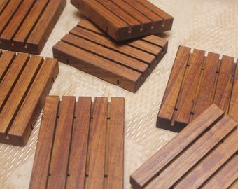 May include: A collection of rectangular wooden soap dishes, each featuring a series of parallel slats with deep grooves. The dishes are crafted from a medium-brown wood with a visible grain pattern, arranged in a scattered layout on a flat surface.