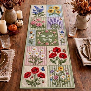 Peut inclure: Un chemin de table matelassé rectangulaire composé d'une grille de panneaux floraux brodés, incluant des tournesols, des roses, de la lavande, des marguerites et des coquelicots. Le panneau central porte le texte The Jonh Family.