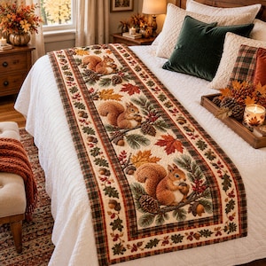 Puede incluir: Un camino de cama rectangular con un panel central de color crema que presenta un patrón repetitivo de ardillas marrones sosteniendo bellotas, piñas y hojas de otoño. El camino está bordeado por un ribete de tela a cuadros en tonos rojos y verdes.