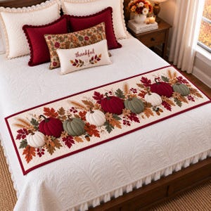 May include: A cream-colored bed runner featuring a repeating pattern of plush, three-dimensional fabric pumpkins in shades of red, green, and white, accented with embroidered autumn leaves, wheat stalks, and acorns on a quilted white background.