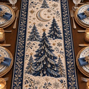Puede incluir: Un camino de mesa rectangular con una escena invernal bordada de pinos azul oscuro, una luna creciente y estrellas doradas sobre un fondo crema. El borde es de tela azul intenso con un intrincado bordado de hojas blancas y doradas.