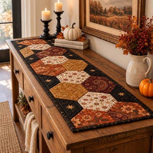 May include: A rectangular quilted table runner featuring a repeating hexagonal pattern in shades of black, burnt orange, mustard yellow, and cream. The fabric displays floral, paisley, and star motifs with intricate stitching throughout the surface.