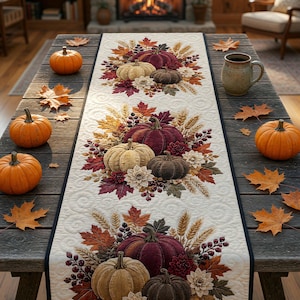 May include: A rectangular quilted table runner featuring a repeating pattern of pumpkins, autumn leaves, wheat stalks, and flowers in shades of cream, burgundy, and brown, with a dark border, displayed on a rustic wooden table with orange pumpkins.