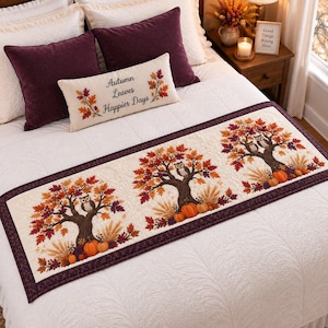 Puede incluir: Un camino de cama rectangular con tres paneles repetidos de árboles otoñales con búhos, calabazas y tallos de trigo. El camino tiene un fondo crema con un borde morado oscuro. Un cojín lumbar a juego lleva la inscripción Autumn Leaves Happier Days.