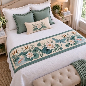 May include: A white bedspread featuring a long rectangular runner decorated with a botanical print of white lotus flowers, green lily pads, cattails, a blue dragonfly, and orange koi fish. The bed includes two sage green ruffled pillows.