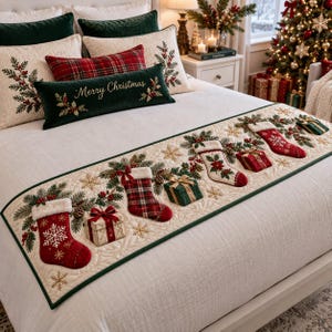 May include: A cream-colored quilted bed runner featuring an embroidered pattern of red Christmas stockings, wrapped gift boxes, pine branches, and gold snowflakes. The runner is displayed on a white bed with matching pillows and a green lumbar pillow.