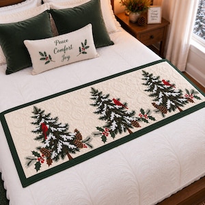 May include: A rectangular bed runner with a cream-colored quilted base featuring a dark green border. The runner displays three printed evergreen trees decorated with snow, pinecones, red holly berries, and red cardinal birds on branches.