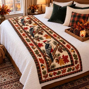 May include: A quilted bed runner featuring a repeating pattern of woodpeckers perched on branches, surrounded by autumn leaves, pinecones, and acorns. The runner has a cream-colored center with a dark plaid border in shades of red, green, and black.