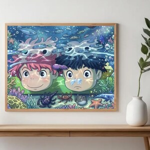 May include: A rectangular wall art print in a light wood frame featuring an animated underwater scene. Two characters with pink and black hair are submerged, surrounded by colourful coral, a crab, a starfish, and various small fish swimming.