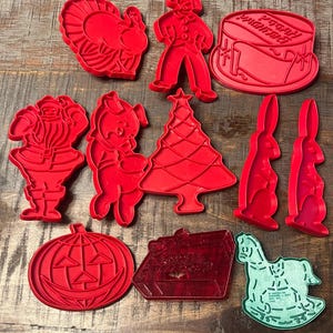 Könnte beinhalten: Eine Sammlung von zehn Kunststoff-Ausstechformen in verschiedenen Formen, darunter ein Truthahn, eine Person, eine Trommel, der Weihnachtsmann, ein Schwein, ein Weihnachtsbaum, zwei Hasen, ein Kürbis, ein Geschenk und ein grünes Schaukelpferd.
