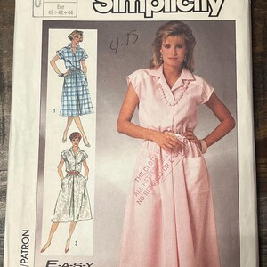 May include: A Simplicity sewing pattern envelope labeled 7475 featuring illustrations and a photograph of a collared, button-front dress with short sleeves, a cinched waist, and large patch pockets. The text includes E-A-S-Y TO SEW and sizes 12-14-16.