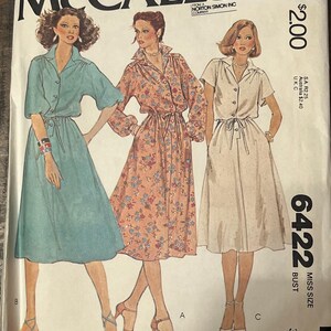 May include: A McCall's 6422 sewing pattern envelope featuring illustrations of three dress variations. The designs include a solid teal dress, a floral print dress with long sleeves, and a solid light-colored dress, all with collared necklines.