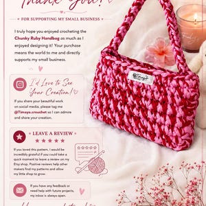 May include: A chunky crochet handbag featuring a variegated pattern of deep ruby red and bright pink yarn. The bag has a single thick braided handle and a small white rectangular label with the text Timaya hand made attached to the front.