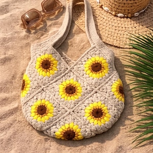 May include: A beige crochet tote bag featuring a repeating sunflower pattern with yellow petals and dark brown centers. The bag has two integrated handles and a textured, knotted yarn construction. The sunflower motifs are arranged in a grid.