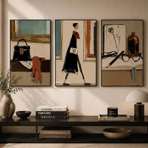 Può includere: Un set di tre stampe artistiche da parete incorniciate con illustrazioni a tema moda. La stampa a sinistra mostra una borsa nera e una sciarpa arancione, quella centrale una persona che cammina con un cappotto nero, quella a destra una bottiglia, occhiali e una matita.