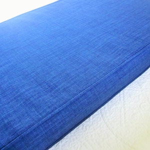 May include: A close-up of a blue denim cushion with a stitched seam. The cushion is made of a soft, textured fabric.
