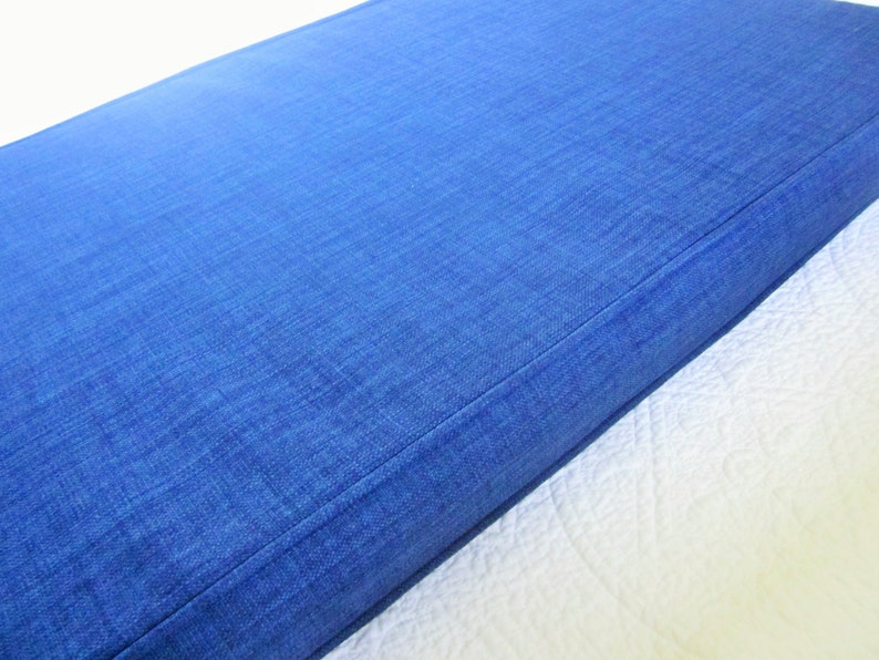 May include: A close-up of a blue denim cushion with a stitched seam. The cushion is made of a soft, textured fabric.