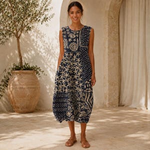 Puede incluir: Un vestido midi sin mangas en azul marino oscuro con un estampado de bloques en color crema de diversas formas florales y geométricas. El vestido tiene un cuello redondo, un corpiño ajustado y una falda suelta y fluida bajo la rodilla.