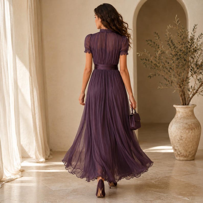 May include: A floor-length deep purple dress featuring a high neckline, short puffed sleeves, and a fitted waist with a wide band. The skirt is made of pleated, sheer fabric that flows to the floor, and the garment is paired with a matching handbag.