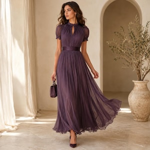 May include: A floor-length dark purple dress featuring a high neckline with a small keyhole cutout, short puffed sleeves, and a fitted waistband. The skirt is made of pleated, flowing fabric that reaches the ankles, paired with a small handbag.