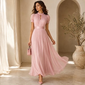 May include: A floor-length dusty pink dress featuring a high neckline with a small keyhole cutout, short puff sleeves, and a fitted waistband. The skirt is made of pleated, flowing fabric that reaches the floor, creating a soft, layered look.