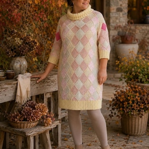 May include: A knee-length knit jumper dress featuring a pastel argyle pattern in shades of yellow, pink, and cream. The garment has a high cowl neckline, three-quarter length sleeves, and ribbed cuffs and hem, paired with light beige leggings.