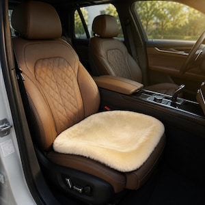 May include: A cream-colored, plush sheepskin seat cover placed on the driver's seat of a vehicle. The car seat is upholstered in brown leather with a diamond-stitched pattern on the backrest and features adjustable electronic seat controls.