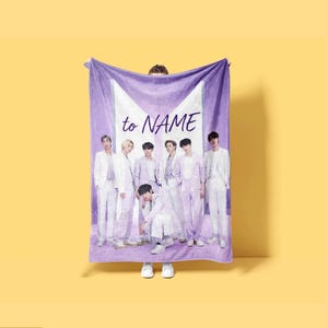 May include: A rectangular purple fleece blanket featuring a large white geometric logo and the text to NAME. The blanket displays a group of seven individuals dressed in light purple suits, arranged in a standing and crouching pose.