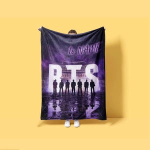 May include: A rectangular plush throw blanket featuring a dark purple and black gradient background with a large white BTS logo. The design includes silhouettes of seven figures standing before a traditional building, with the text to NAME printed above.