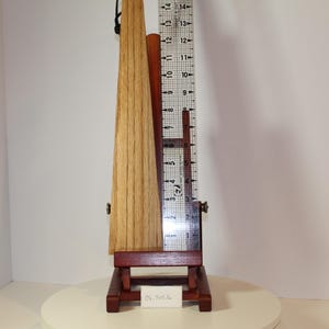May include: A light brown wooden wedge-shaped object displayed on a dark reddish-brown wooden easel. A clear plastic ruler is positioned vertically against the object, showing a height measurement of approximately 14 inches from base to top.