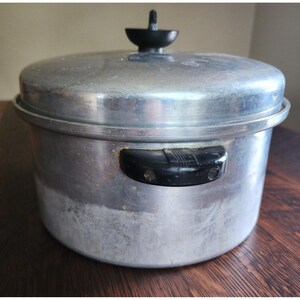 May include: A round, silver-colored aluminum cooking pot with a matching lid. The pot features two black, horizontal side handles with visible screws and a black, knob-style handle centered on the lid. The metal surface shows signs of wear.