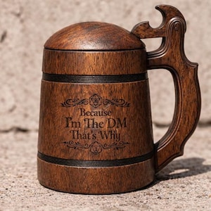 Op de afbeelding: Een donkerbruine houten bierpul met een deksel en een handvat met een geïntegreerde flesopener. De voorzijde is gegraveerd met de tekst "Because I'm The DM That's Why", omringd door decoratieve krullen en twee twintigzijdige dobbelsteeniconen.