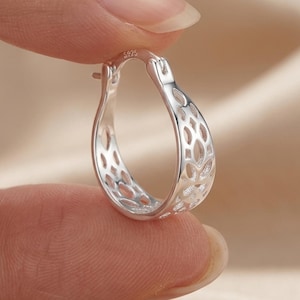 May include: A silver hoop earring featuring an intricate openwork lattice pattern throughout its structure. The metal surface is polished and reflective, with the hallmark S925 clearly engraved on the top inner edge of the earring hoop.