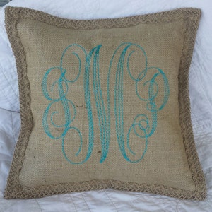 May include: A burlap pillow with a turquoise embroidered monogram. The pillow has a burlap trim.