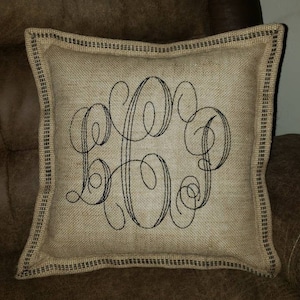 May include: A burlap pillow with a black embroidered monogram. The pillow has a black and white checkered trim.