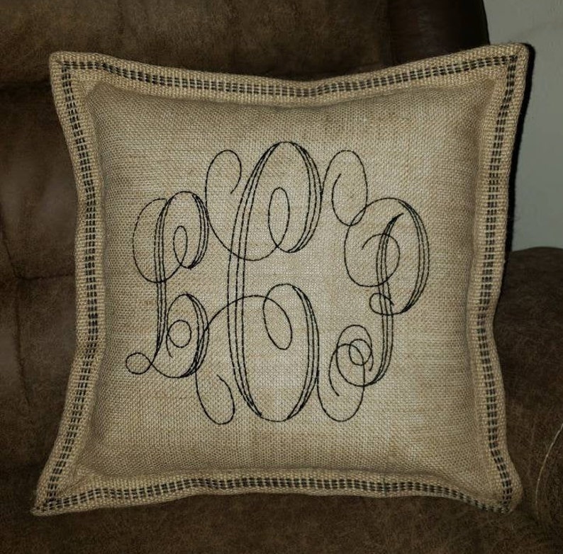 May include: A burlap pillow with a black embroidered monogram. The pillow has a black and white checkered trim.