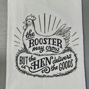 May include: White kitchen towel with a black illustration of a hen and the text "the ROOSTER may crow BUT the HEN delivers the GOODS". The towel is rectangular and made of a soft fabric.