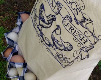 May include: A white canvas egg carrier with blue and white checked pockets. The carrier has an embroidered design of two chickens and a banner that reads "Farm Fresh Eggs".