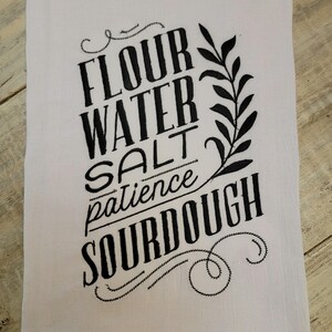 May include: White kitchen towel with black embroidered text that reads "Flour Water Salt Patience Sourdough".