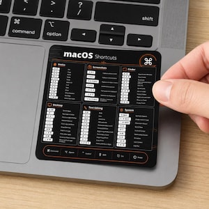 May include: A black rectangular sticker featuring a white macOS Shortcuts reference guide with sections for Basics, Screenshots, Finder, Desktop, Text Editing, and System. The sticker displays various keyboard key combinations and their functions.