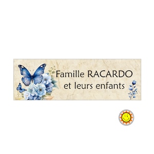 Può includere: Un cartello in legno rustico con una farfalla blu e fiori, con il testo "Famille RACARDO et leurs enfants".
