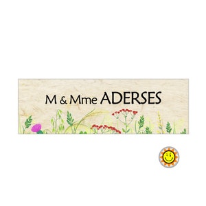 Pode incluir: Uma placa de madeira rústica com fundo bege e borda verde. A placa tem um design floral com uma variedade de flores e ervas. O texto "M & Mme ADERSES" está impresso em preto na placa.