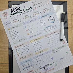 May include: A white ADHD Command Center planner sheet with a black dry-erase marker. The layout includes sections for daily check-ins, top priorities, focus sessions, distraction checks, evening shutdown, hydration tracking, and notes with colourful icons.