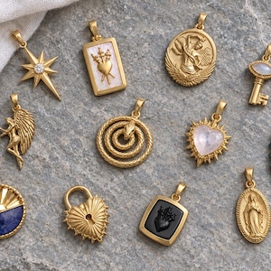 May include: A collection of eleven gold-toned metal pendants featuring diverse designs including a starburst with a clear stone, a heart with three swords, an angel, a key, a coiled snake, a heart with a stone, a wing, a sun, a lock, and figures.