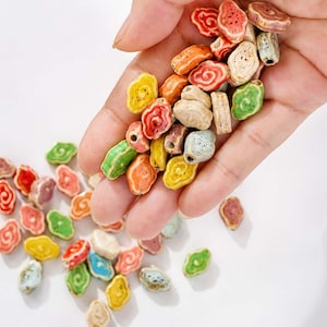 May include: A collection of small, irregularly shaped ceramic beads featuring a central hole and a swirling, embossed pattern. The beads are finished in a variety of vibrant colors including red, orange, yellow, green, blue, and off-white tones.